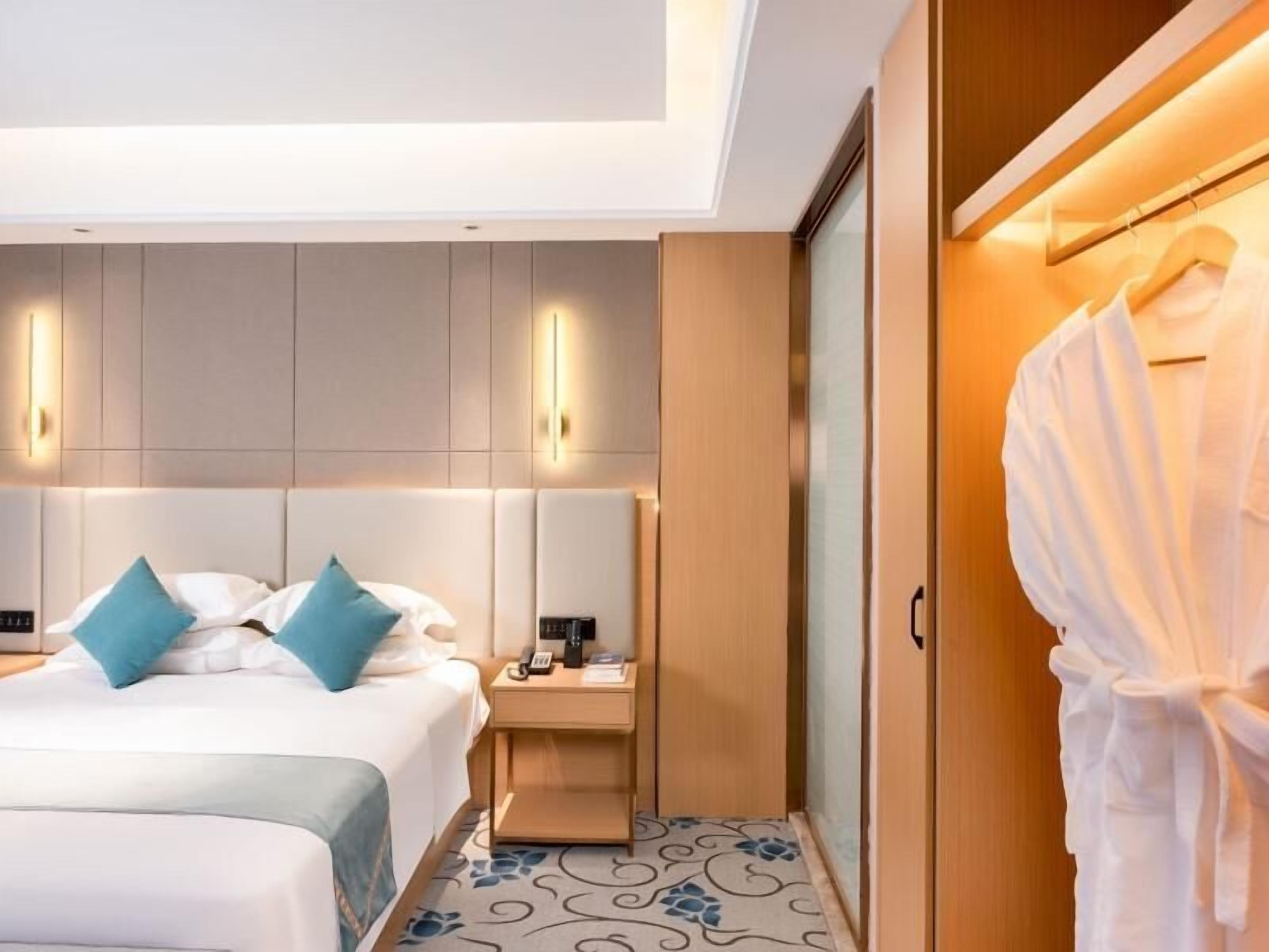 Een hotelkamer met een bed, nachtkastje, een hangende badjas en een kledingkast.