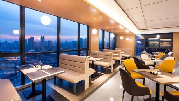A modern dining area with high tables and benches, large windows offering a city view, and pendant lighting. - Greentree Eastern Tongling City Beijing West Road Big Dipper City Hotel (Tongling)