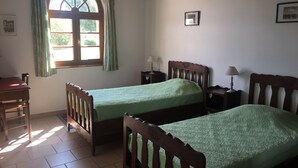 Quarto com duas camas de madeira, uma escrivaninha e janela com cortinas.