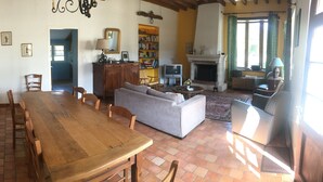 Uma sala de estar ampla com uma mesa de jantar de madeira, um sofá e uma lareira.