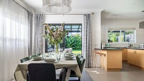Ein Essbereich mit einem Tisch für sechs Personen, einer Blumenvase und Blick auf den Garten durch das Fenster.