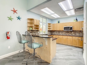 A modern kitchen with a central island, bar stools, wooden cabinets, a microwave, and a fire extinguisher.