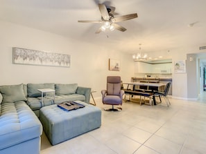 A modern living room with a sectional sofa, a dining area with a table and chairs, a ceiling fan, and artwork on the walls.