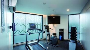 A modern gym with a treadmill, elliptical, stationary bike, and a set of dumbbells.