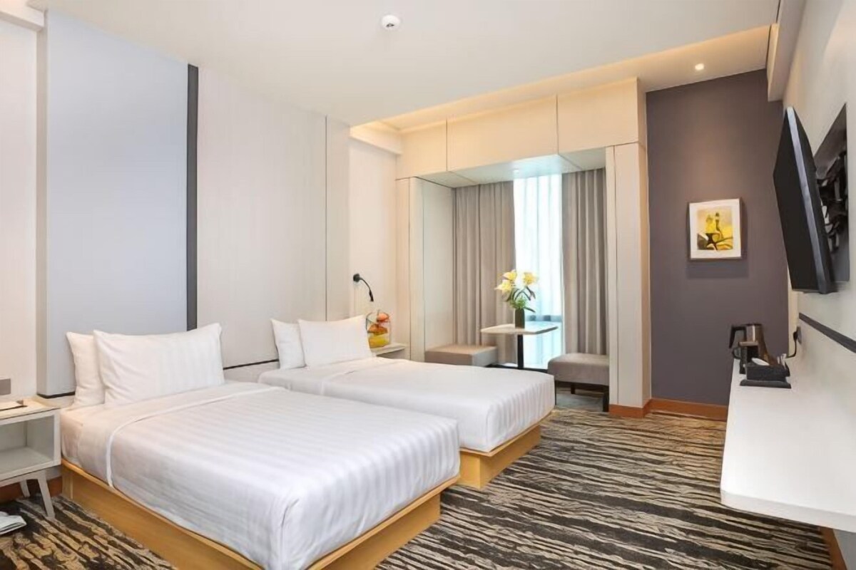A hotel room with two beds, a desk, a chair, a TV, and a window with curtains.