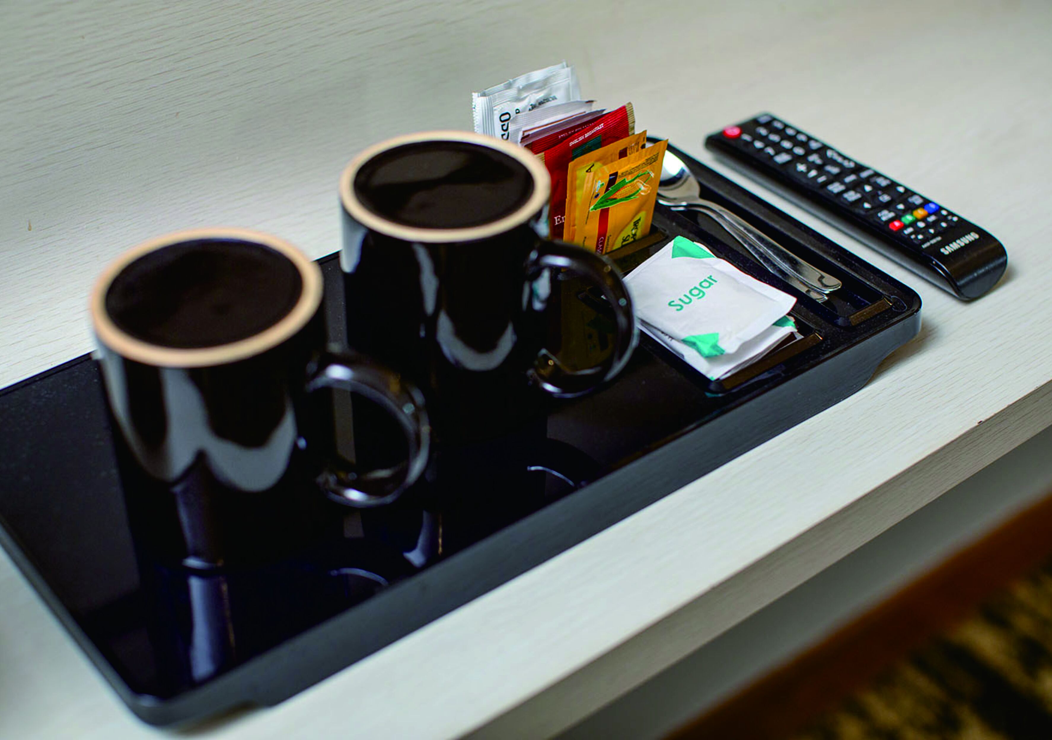 A tray with two black cups, a remote control, and some snacks.