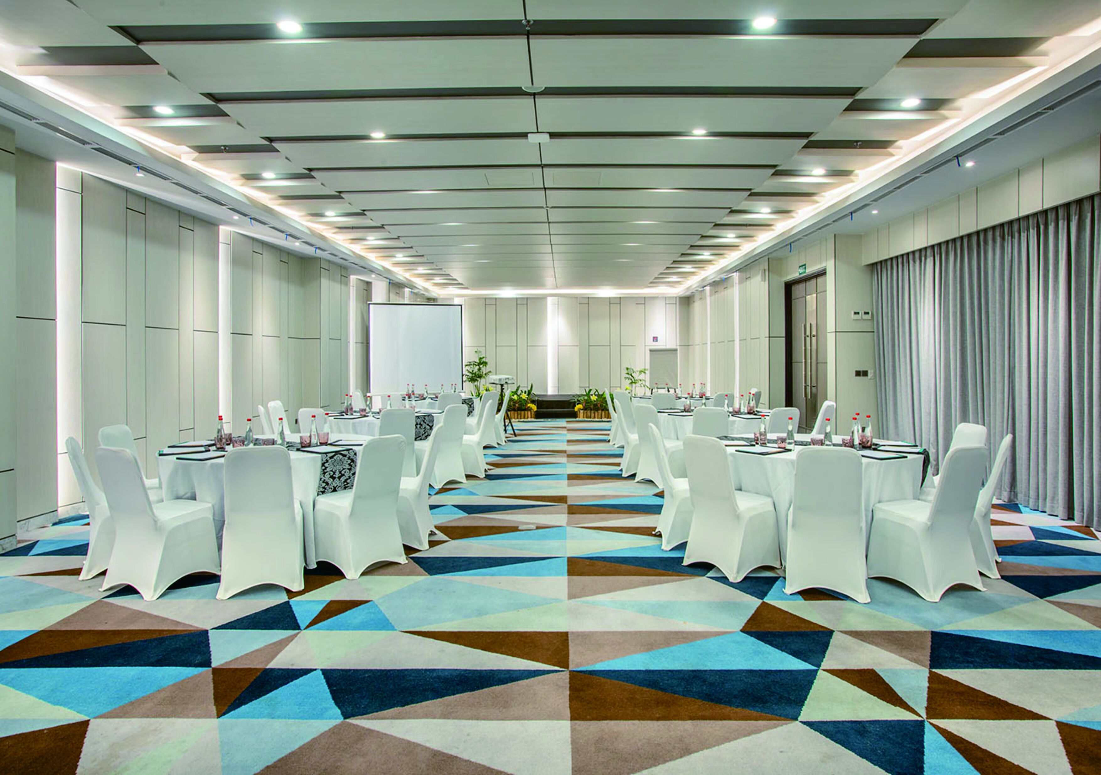 Une salle de conférence avec des chaises et des tables blanches, une moquette à motifs et un plafond doté d’un éclairage encastré.