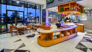 A modern hotel lobby with a marble floor, a reception desk with a plant, and a seating area with wooden chairs and tables. - THE 1O1 Jakarta Airport CBC (Tangerang)