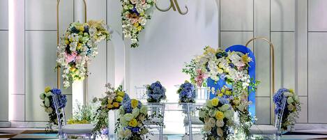 A reception area with a white backdrop, a blue door, and clear chairs adorned with floral arrangements.