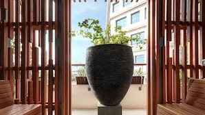 A wooden bench and a large planter in the center of a corridor with a view of a building in the background. - THE 1O1 Jakarta Airport CBC (Tangerang)