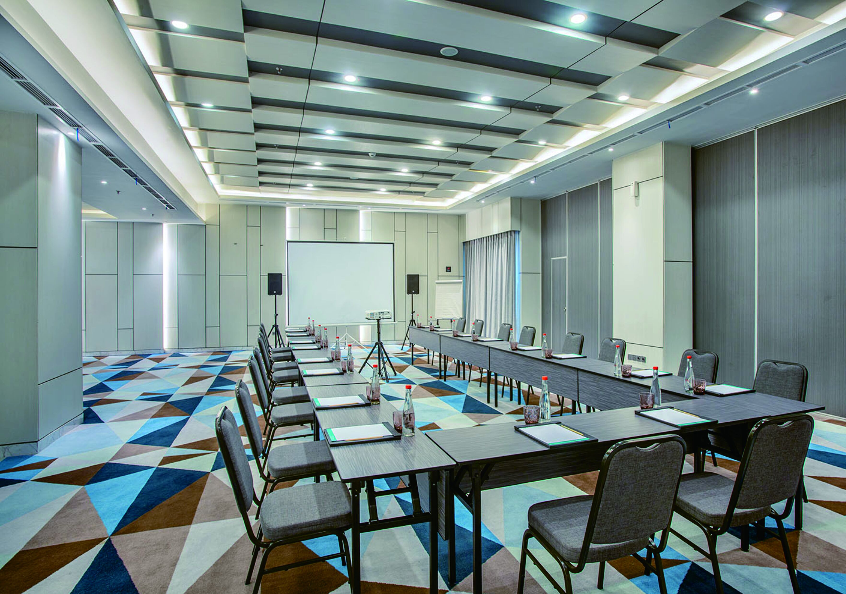 A conference room with a long table, chairs, and a projector screen.