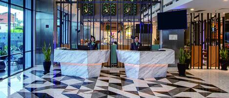 A hotel lobby with a geometric patterned floor, two reception desks, and a large window overlooking the street.