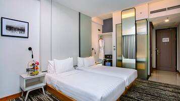 A hotel room with two beds, a bedside table with a fruit basket, a mirror, and a robe hanging on a rack.