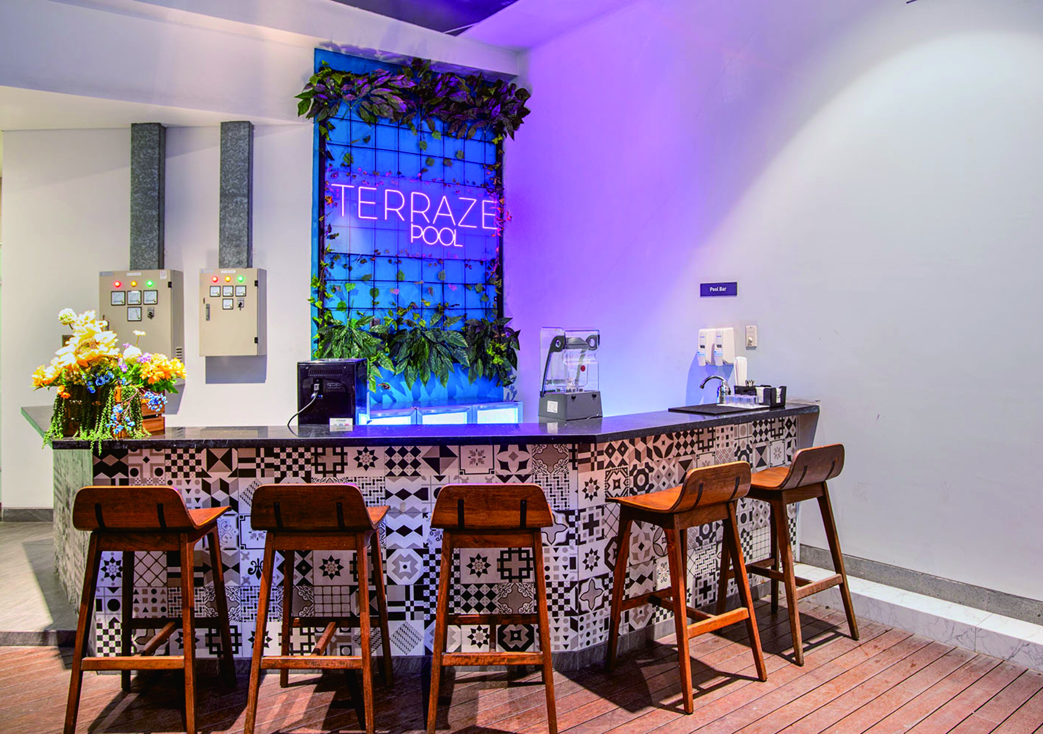 A bar area with a neon sign reading "TERRAZE POOL", bar stools, a counter with a patterned tile backsplash, and a plant decoration.