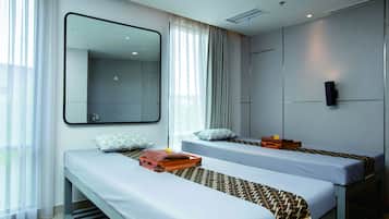 Two single beds with matching headboards and throw blankets, a wooden bench, and a large mirror.