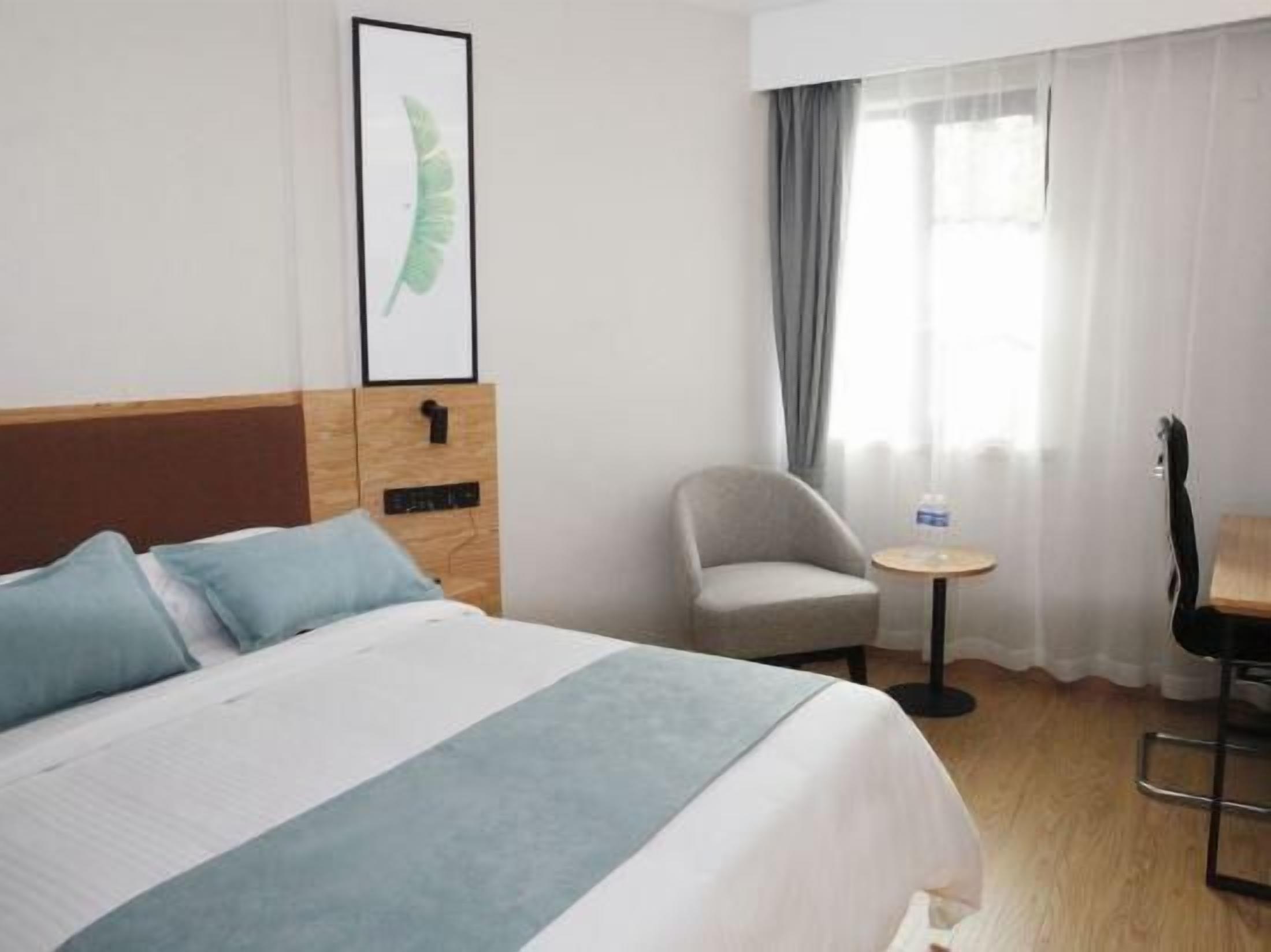 A hotel room with a bed, a chair, a small table, and a window with curtains.