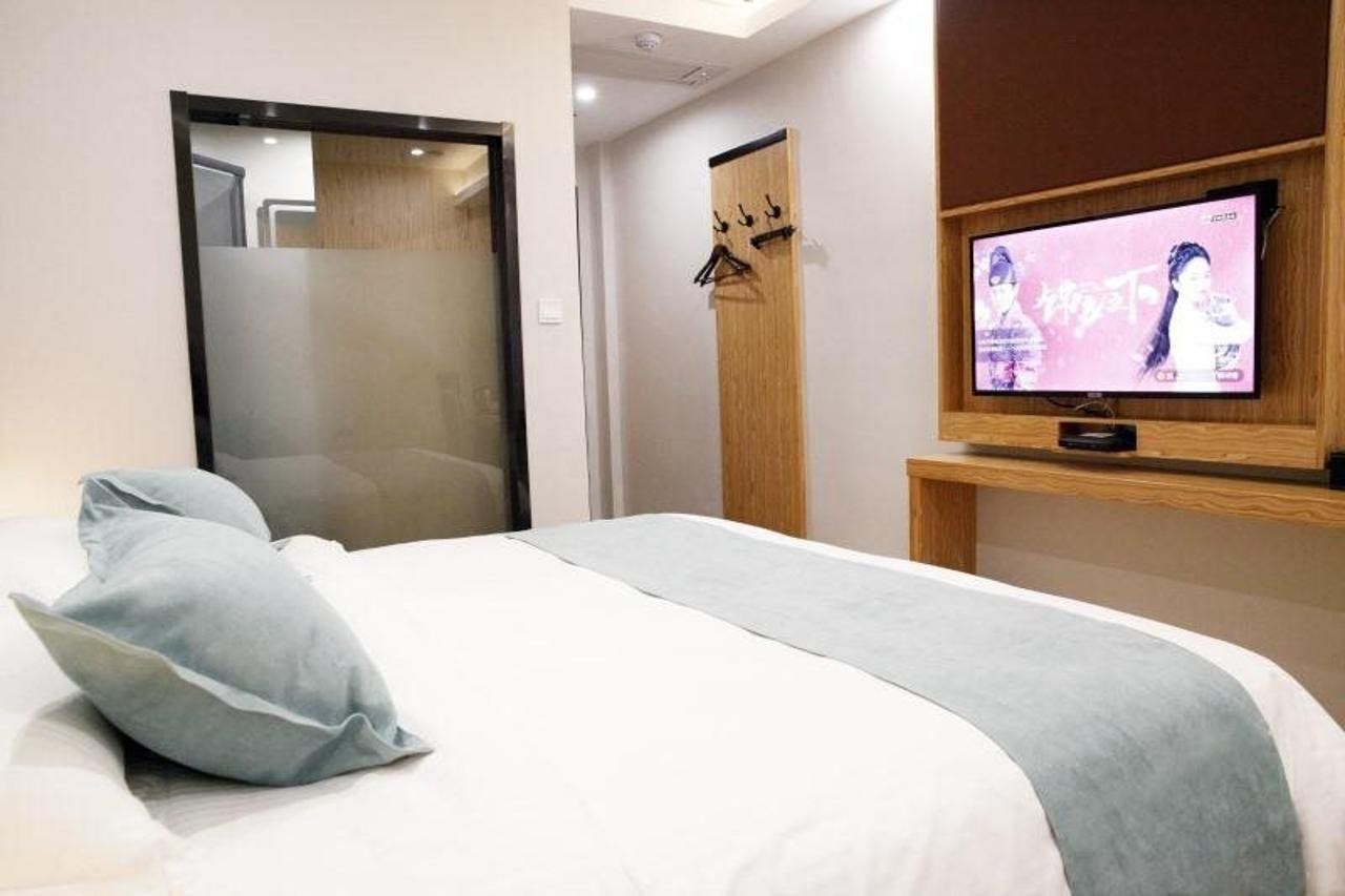 Ein Hotelzimmer mit einem Bett, einem an einer Holzablage montierten Fernseher und einer Tür mit satinierten Glasscheiben.