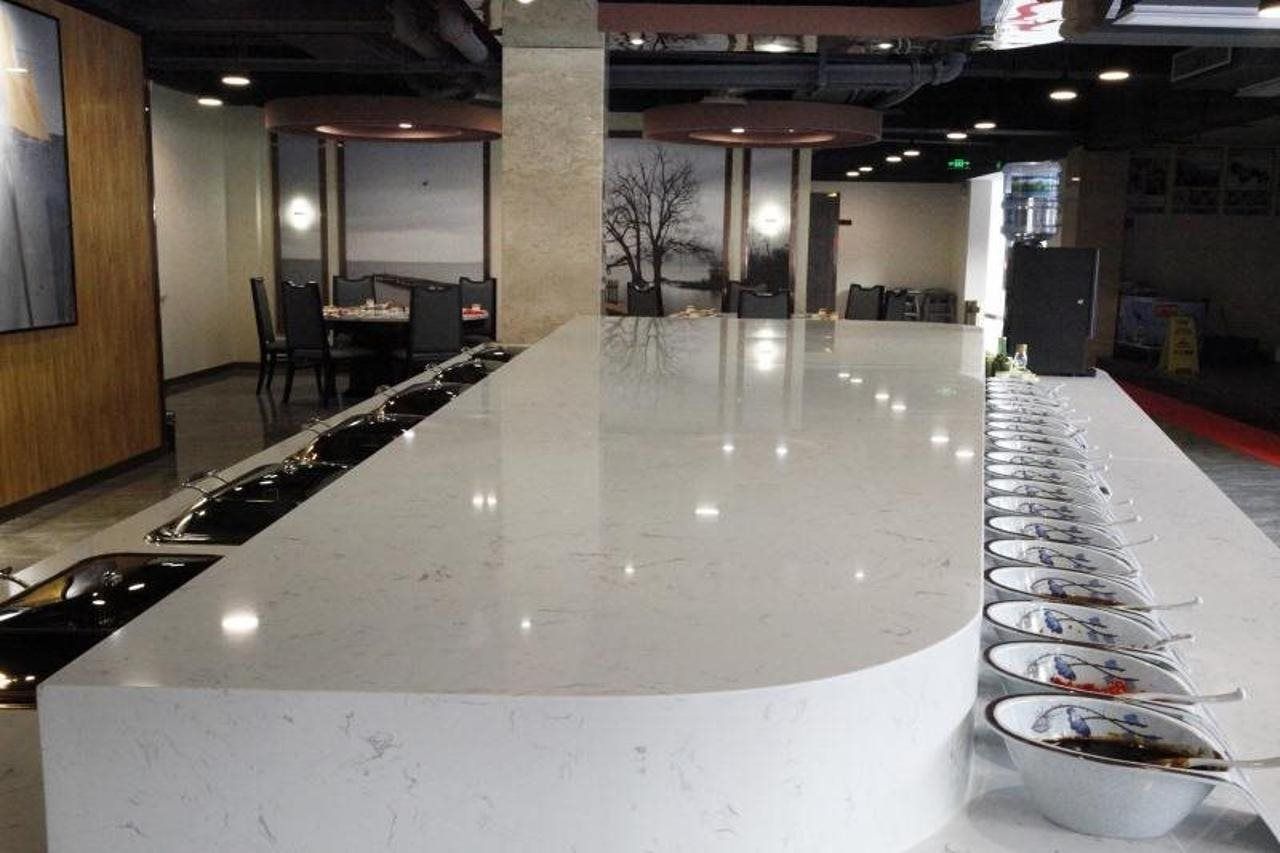 A long, white marble counter with multiple bowls and spoons, likely for a buffet.