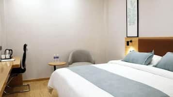 A hotel room with a bed, a desk with a chair, a small table, and a wall-mounted artwork.