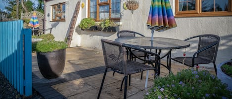A patio with a table and chairs, a hanging chair, and a rainbow umbrella.
