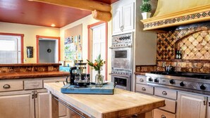 Una cocina con armarios de madera, cafetera, un jarrón con flores y salpicadero de azulejos.