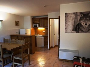 Eine kompakte Küche mit Holzausstattung, einer Mikrowelle, einem Spülbecken und einem Geschirrspüler. Ein Esstisch mit Stühlen und ein Bild eines Wolfs an der Wand.