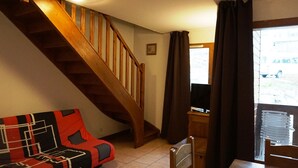 Ein Wohnzimmer mit einer Holztreppe, einem Sofa mit geometrischem Muster, einem Holzstuhl und einem Fernseher auf einem Holztisch.
