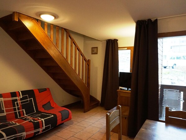 Ein Wohnzimmer mit einer Holztreppe, einem Sofa mit geometrischem Muster, einem Holzstuhl und einem Fernseher auf einem Holztisch.