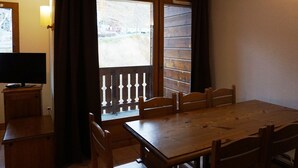 Ein Zimmer mit einem Holztisch und -stühlen, einem Fernseher auf einem Schrank und einem Fenster mit Vorhängen.