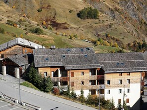 Ein mehrstöckiges Gebäude mit Holzfassade und Balkonen, gelegen in einer hügeligen Landschaft mit Herbstlaub.