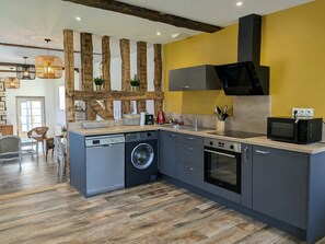 A modern kitchen with grey cabinetry, a washing machine, an oven, and a microwave.