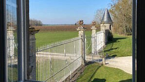 Blick auf ein Anwesen mit weißem Metallzaun, einem Steinhaus mit Kegeldach und einem grünen Feld im Hintergrund.