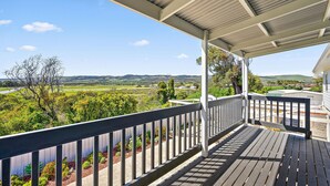 A covered outdoor area with a wooden deck and railing, overlooking a scenic landscape with hills and greenery.