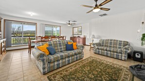 A spacious living room with a large sofa set, a dining area, and a balcony with a view.