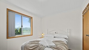 A bedroom with a bed, a window with curtains, a bedside table with a lamp, and a wooden door.
