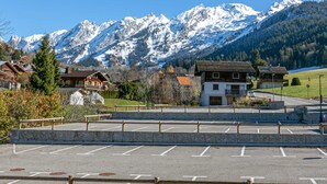A parking area with a view of snow-covered mountains and traditional wooden houses.