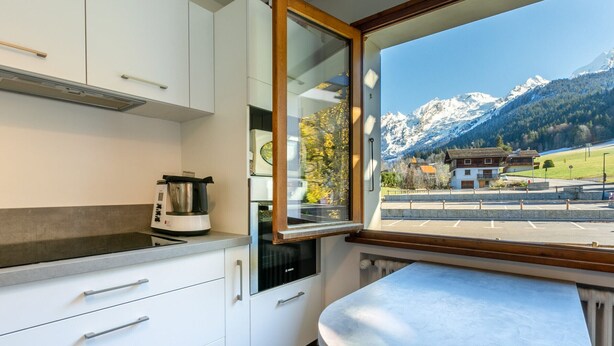 A modern kitchen with white cabinets, a built-in stove, and a window overlooking a mountain landscape.