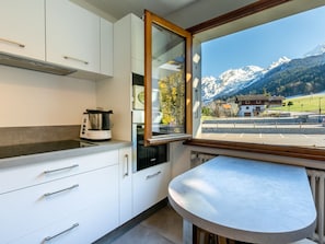 Cozinha moderna com armários brancos, fogão embutido e janela com vista para uma paisagem de montanha.