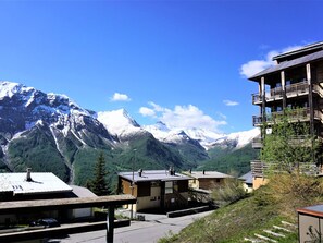 Une station de montagne avec des bâtiments de style chalet, un parking et une vue sur des montagnes enneigées.
