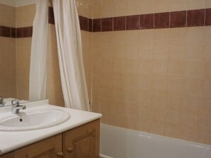 Une salle de bain avec un lavabo blanc, des meubles en bois et une baignoire.
