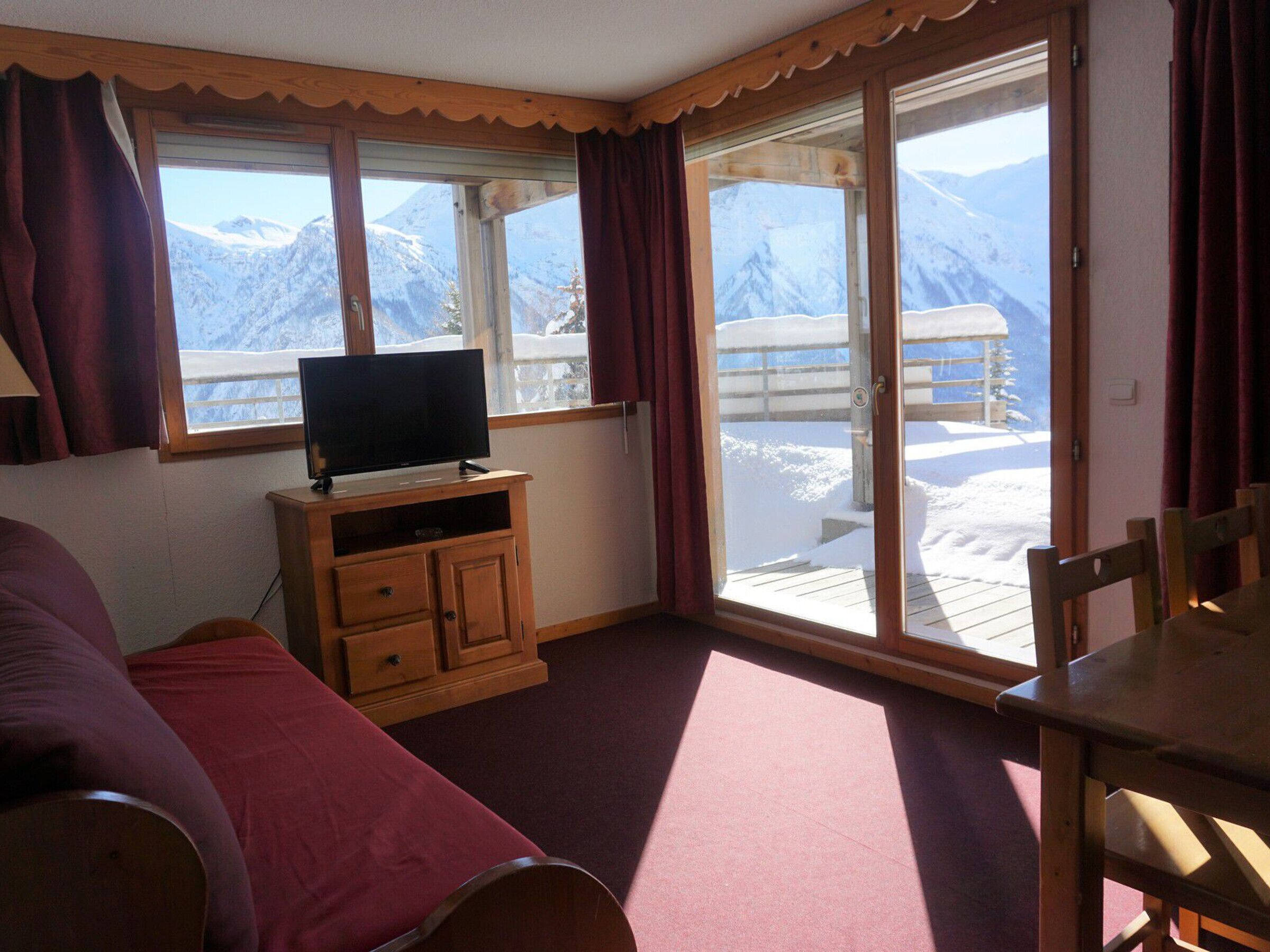 Ein Zimmer mit Fernseher auf einem Holzboden, einem Bett, einem Tisch und großen Fenstern mit Blick auf die Berge.