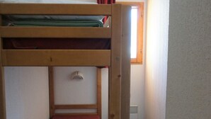 Ett rum med en våningssäng, där den ena madrassen är röd och den andra vit. Det finns ett fönster med gardiner och ett element på väggen.