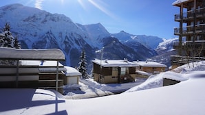 En snötäckt bergsby med hus i chaletstil, en klar himmel och en sol som skiner över bergstopparna.