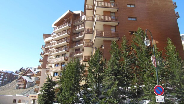 Een meerhoog gebouw met balkons, waarschijnlijk een hotel of appartementencomplex, omringd door bomen en een heldere lucht.