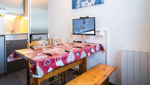 Een eethoek met een houten tafel gedekt voor vier personen, een bank en een televisiescherm waarop een sportevenement te zien is.