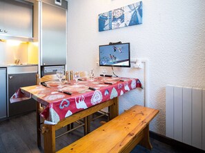 A dining area with a wooden table set for four, a bench, and a television screen displaying a sports event. - Cozy studio in the heart of Val Thorens for 2 people (Val Thorens)
