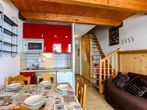 Uma cozinha compacta com armários vermelhos, micro-ondas e área de jantar com mesa posta para quatro pessoas.