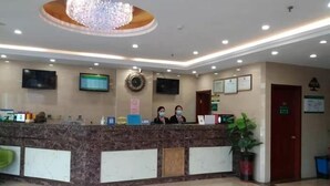 A hotel reception area with a marble counter, two monitors, a chandelier, and a potted plant. - Greentree Alliance Beijing Daxing District Yizhuang Old Palace Metro Station Hotel (Beijing)