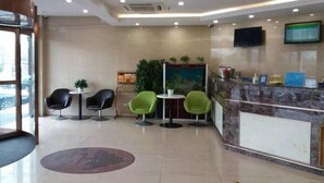 A hotel lobby with a reception desk, two green chairs, a black chair, a chandelier, and a large window. - Greentree Alliance Beijing Daxing District Yizhuang Old Palace Metro Station Hotel (Beijing)
