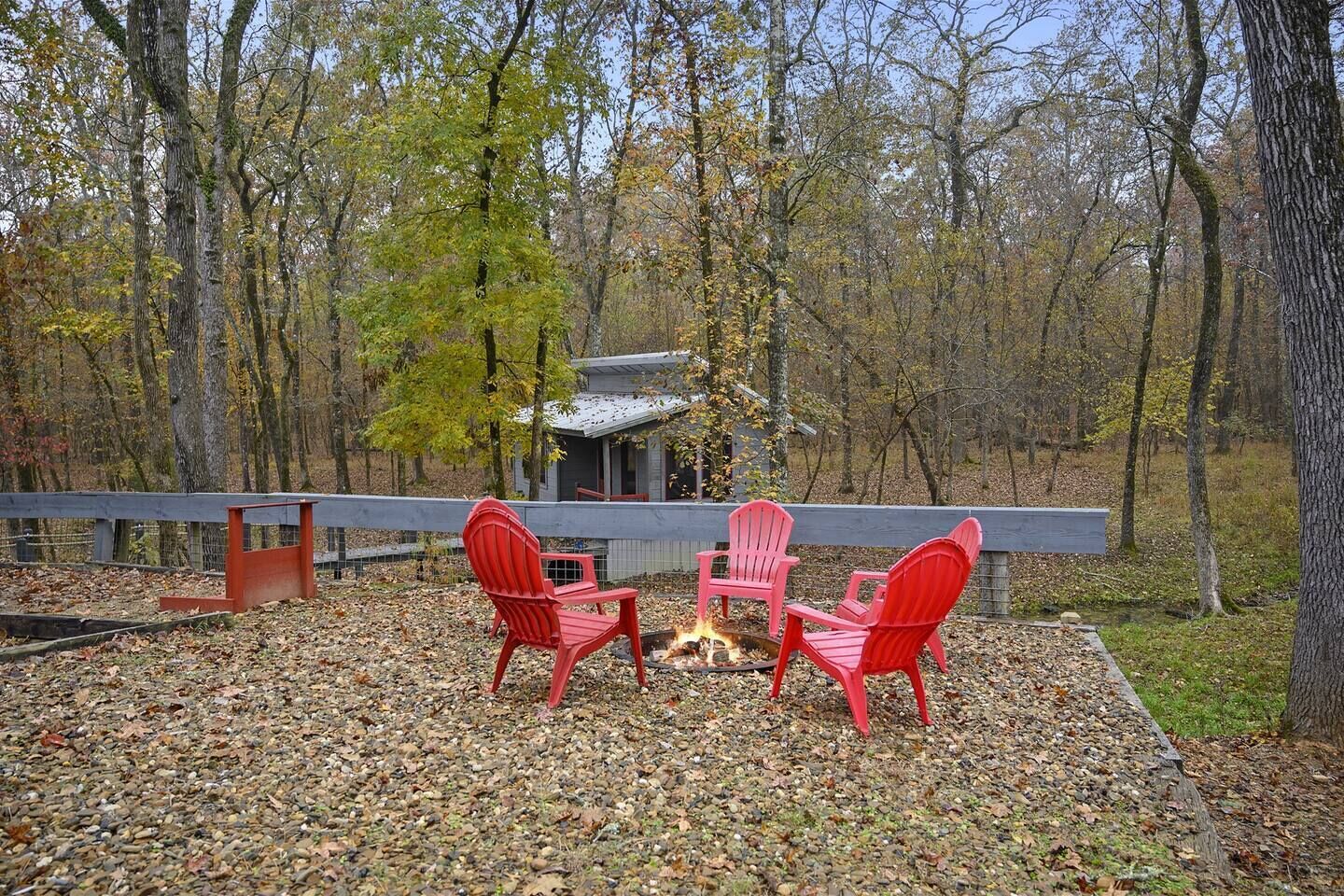A wooden deck with three red Adirondack chairs facing a small fire pit.